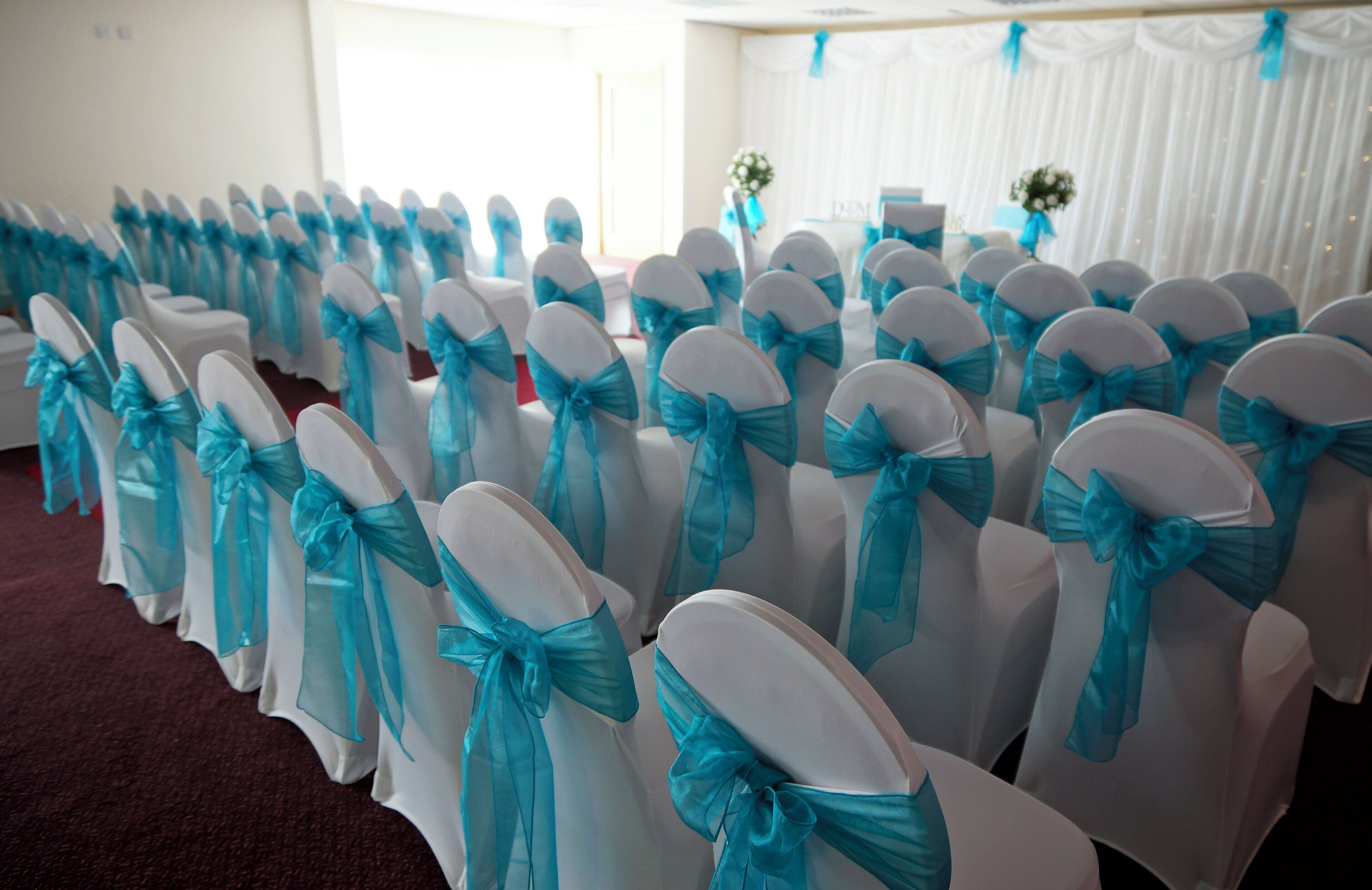 Rows of chairs with white covers and blue sashes.