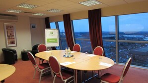 A conference room with a large table, red chairs, a whiteboard, and a view of a cityscape through large windows. - Holiday Inn Birmingham North - Cannock by IHG (Cannock)
