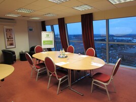 Un salón de conferencias con una gran mesa, sillas rojas, una pizarra y vistas a un paisaje urbano a través de amplios ventanales.