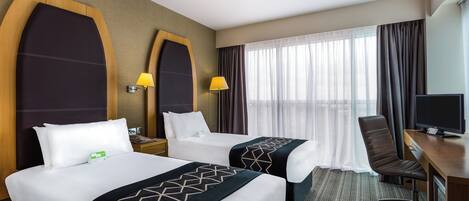 A hotel room with two beds, a desk, a chair, a TV, and a window with curtains.