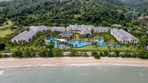 Une vue aérienne d’un complexe hôtelier comprenant plusieurs bâtiments, un grand espace piscine et une plage.