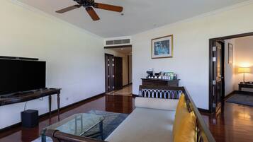 Un salón espacioso con ventilador de techo, televisor de pantalla plana, una mesa de centro de vidrio y un sofá.