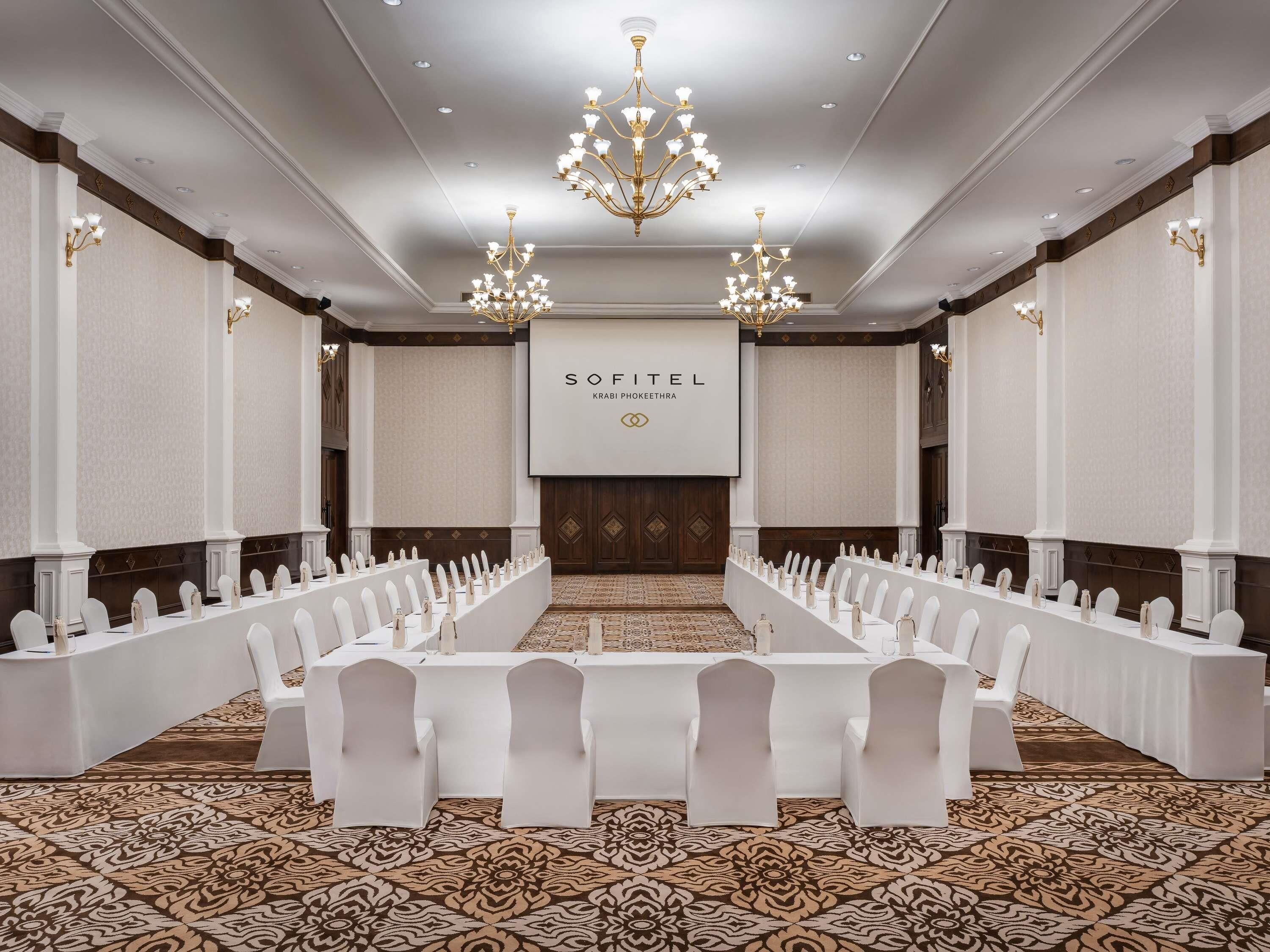 A conference room with a long table, white chairs, chandeliers, and a 'SOFITEL' sign.
