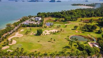 Vista aérea de un campo de golf con un club de campo, obstáculos acuáticos y palmeras.