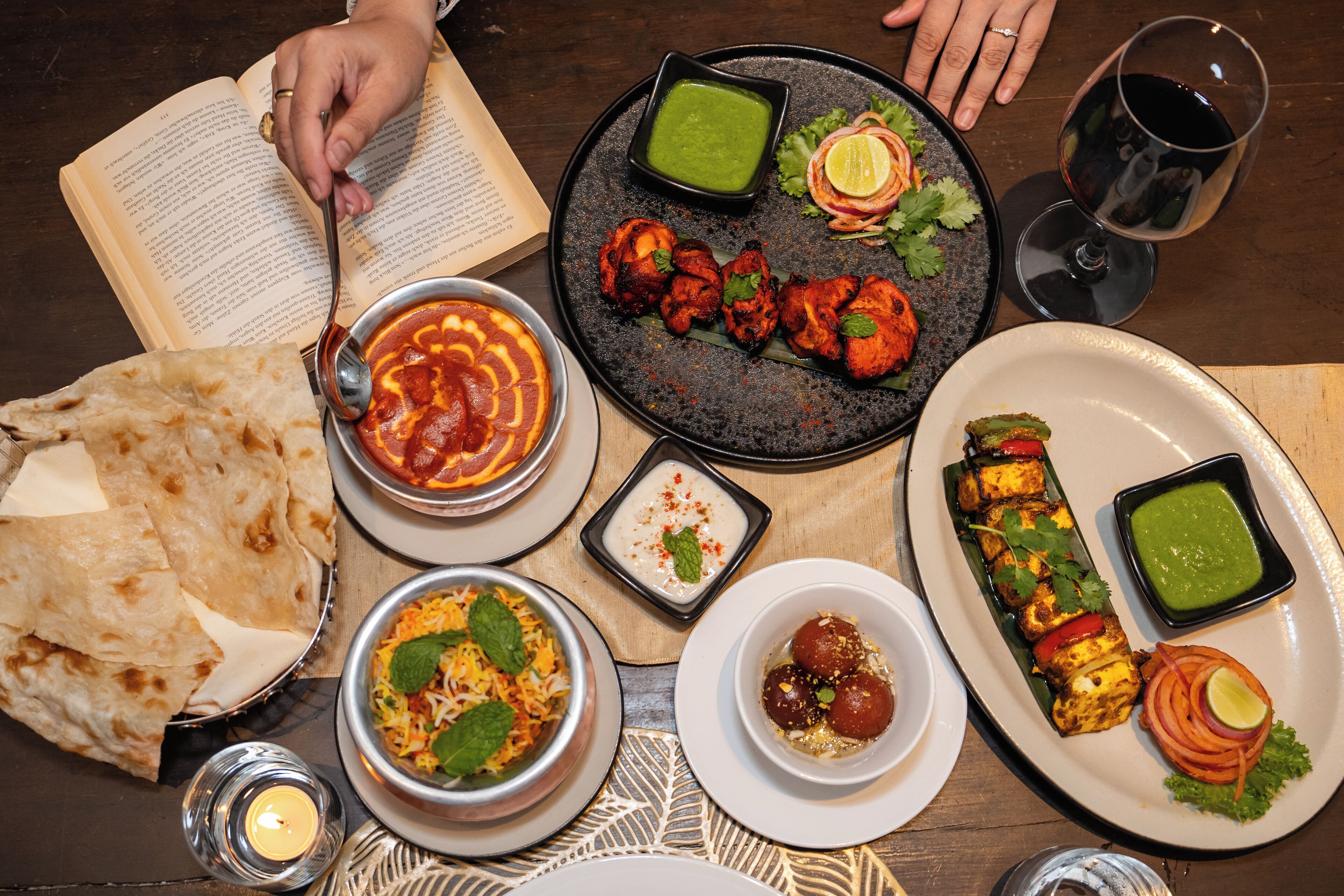 A table with various dishes, including naan bread, a bowl of rice, and a plate of tandoori chicken.