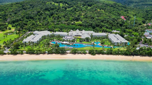 Une vue aérienne d’un complexe hôtelier comprenant plusieurs bâtiments, une grande piscine et une plage.