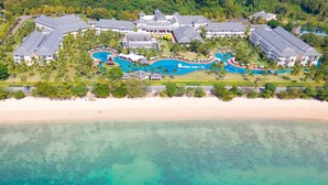 Vista aérea de un resort con varias construcciones, una piscina central grande y una playa.