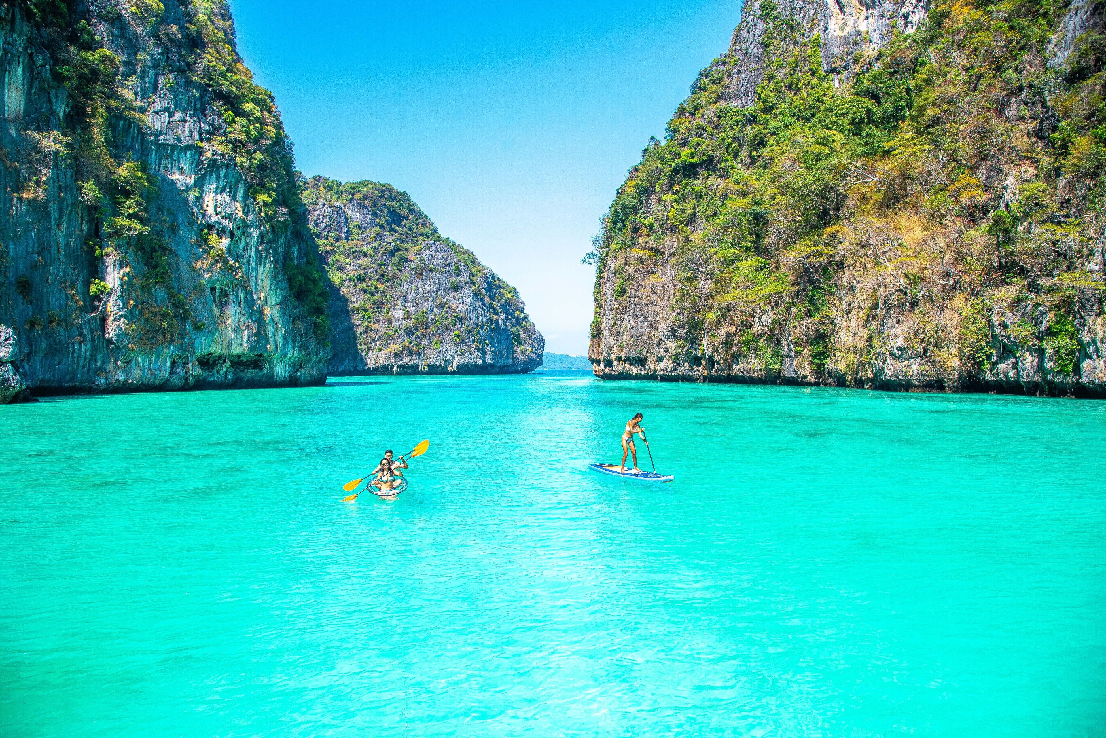 A clear turquoise sea with two paddleboards, surrounded by rocky cliffs.