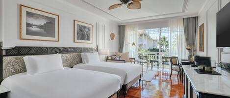 Habitación de hotel con dos camas, un balcón con vistas y ventilador de techo, además de televisión.