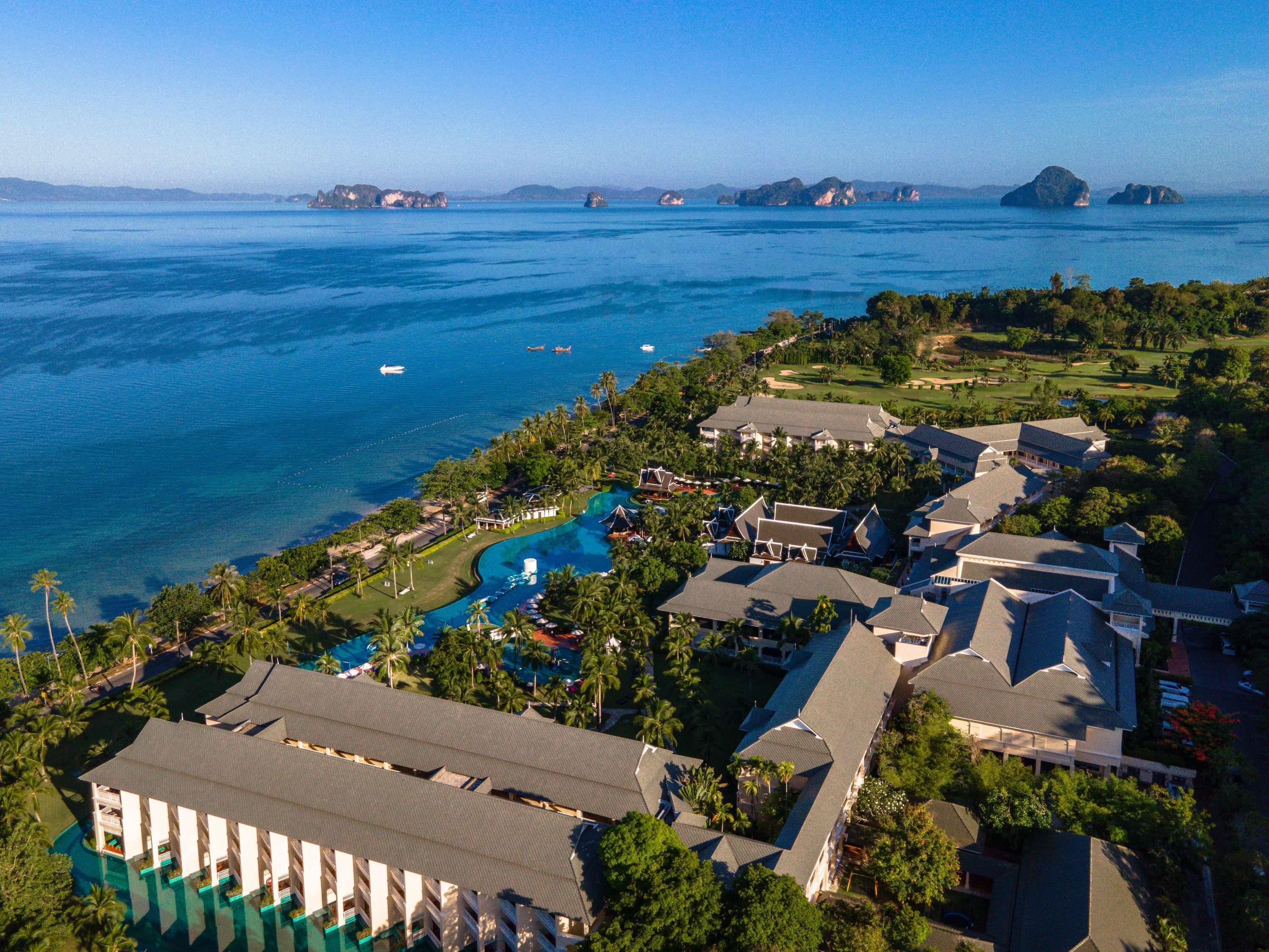 An aerial view of a resort with multiple buildings, a swimming pool, and a view of the ocean.