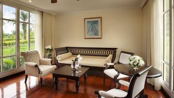 Una habitación amplia con un gran ventanal, un ventilador de techo, un sofá, sillones, una mesa de centro y una mesa de comedor.