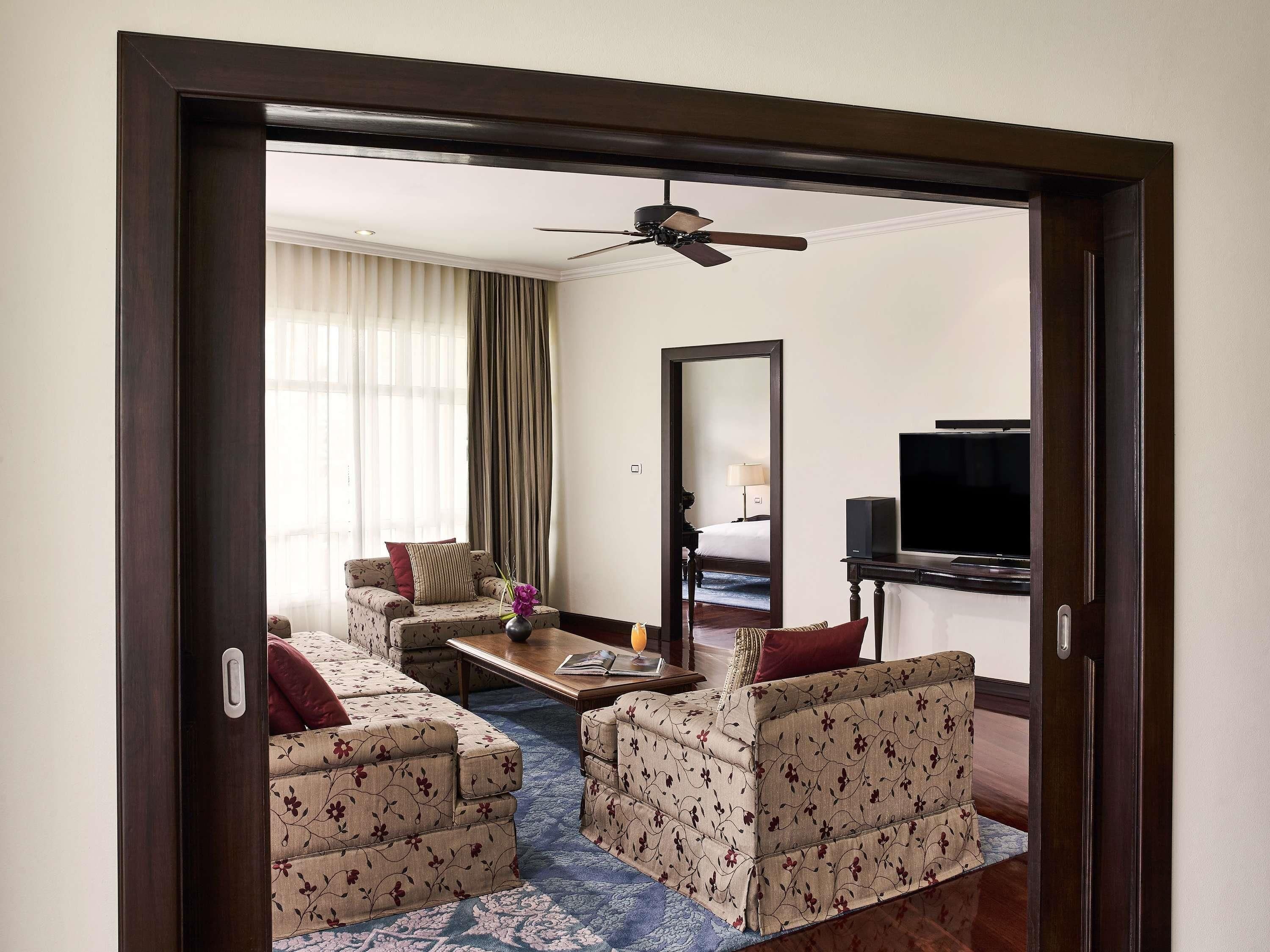 Habitación de hotel con sofá, una mesa de centro, televisión, ventilador de techo y un espejo grande.