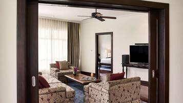 Habitación de hotel con sofá, una mesa de centro, televisión, ventilador de techo y un espejo grande.