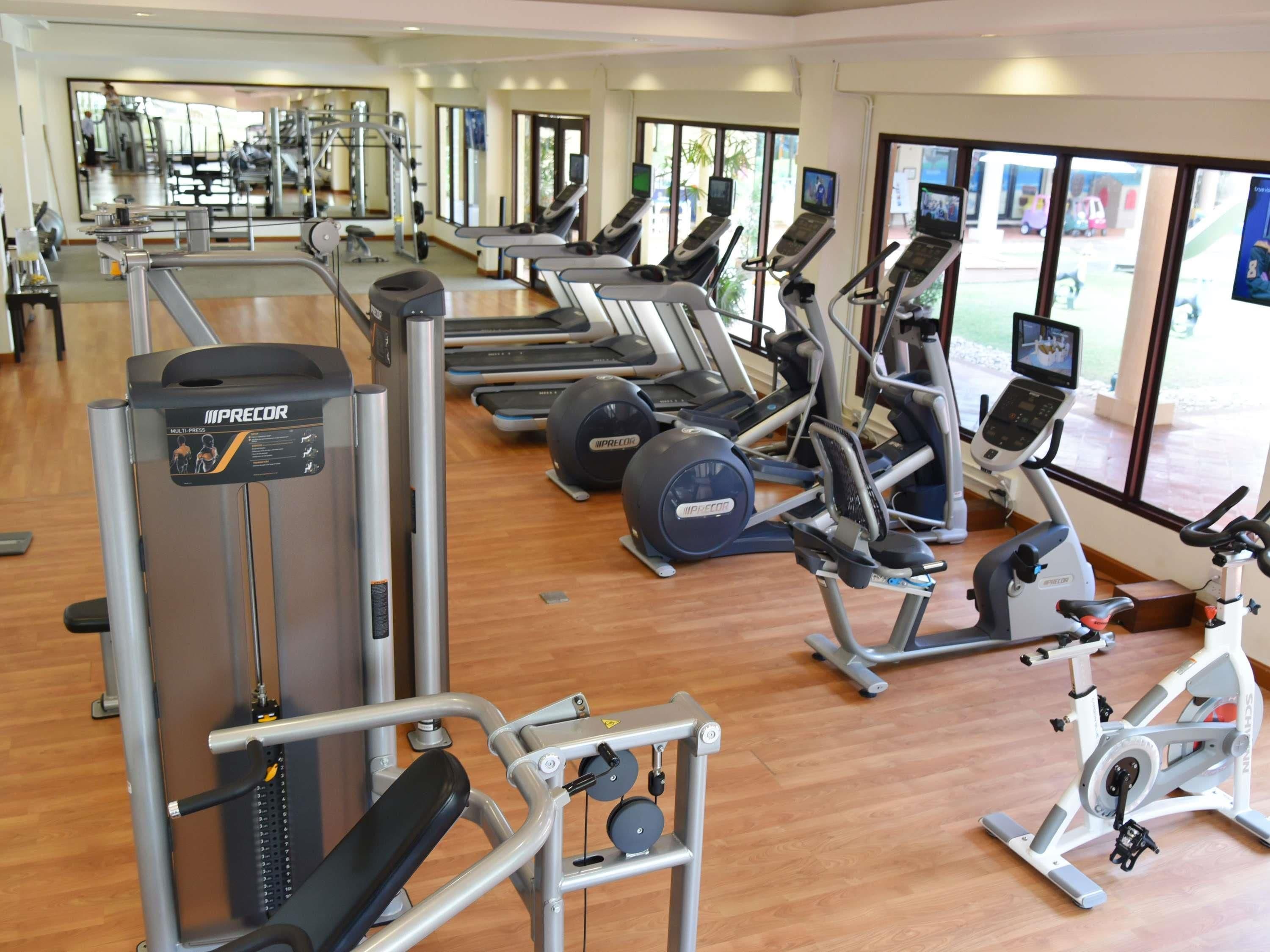 A gym with various exercise machines, including treadmills and weight stations, with large windows providing natural light.