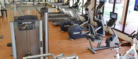 A gym with various exercise machines, including treadmills and weight stations, with large windows providing natural light.