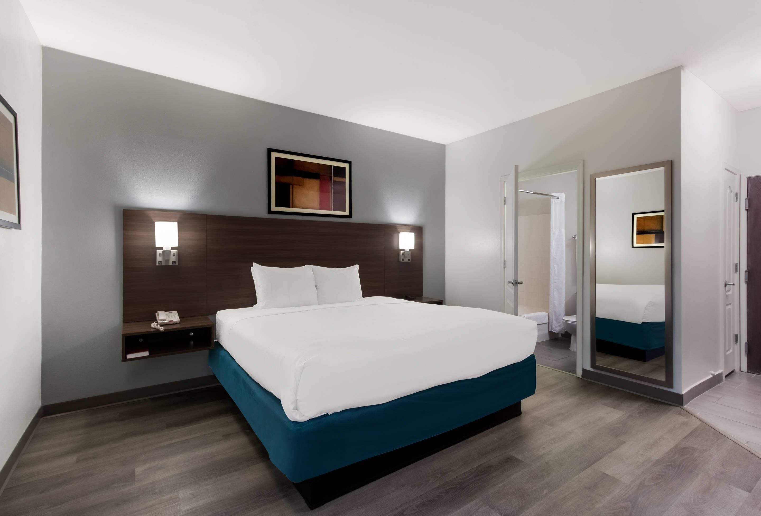Ein Hotelzimmer mit einem großen Bett, Nachttischen, einem Spiegel und einer Tür zu einem Badezimmer.