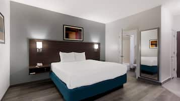 Ein Hotelzimmer mit einem großen Bett, Nachttischen, einem Spiegel und einer Tür zu einem Badezimmer.