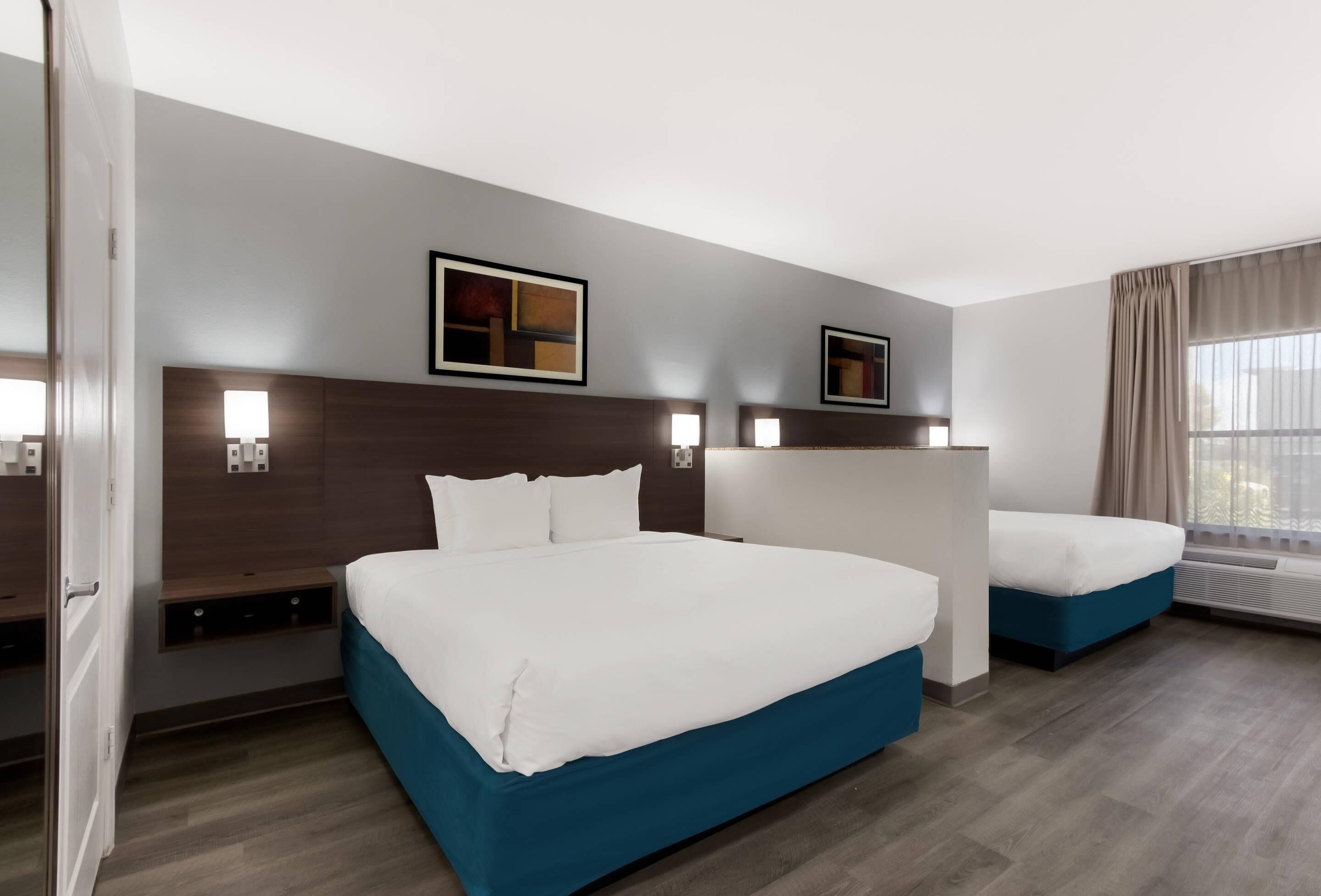 Habitación de hotel con dos camas, un ventanal con cortinas e iluminación empotrada.