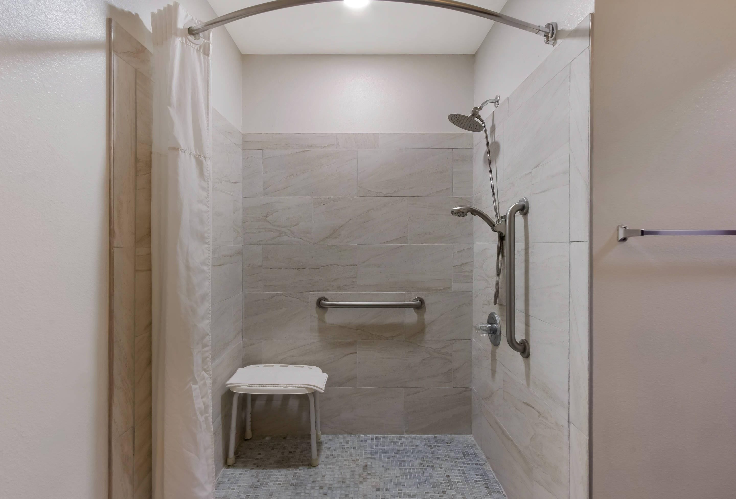A small, enclosed shower area with a grab bar, a bench, and a showerhead.