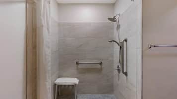 A small, enclosed shower area with a grab bar, a bench, and a showerhead.