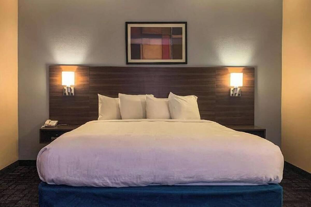 A hotel room with a large bed, two bedside lamps, a framed artwork above the bed, and a telephone on the nightstand.