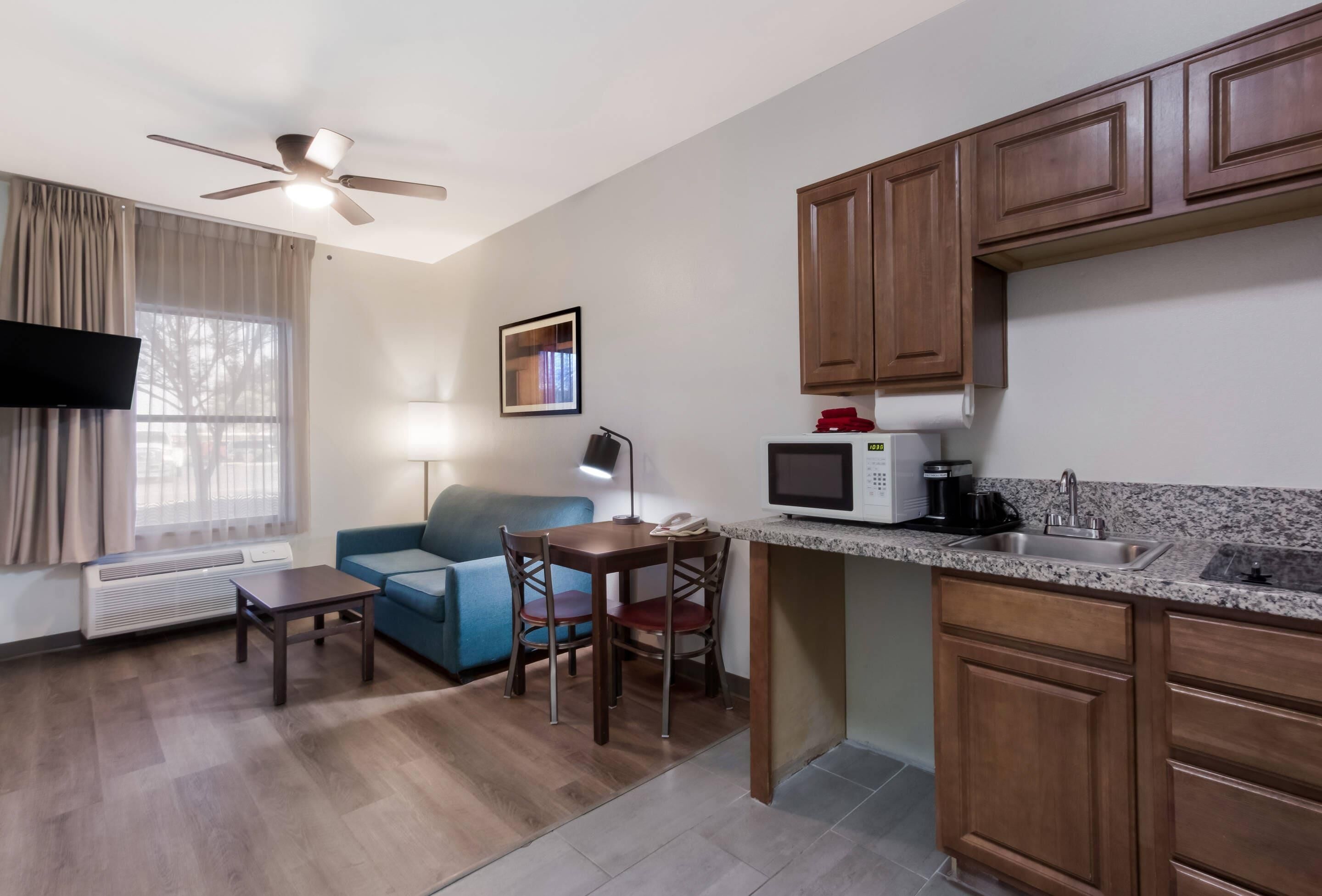 A compact living space with a kitchenette, a dining area with a table and chairs, a sofa, a ceiling fan, and a window with curtains.
