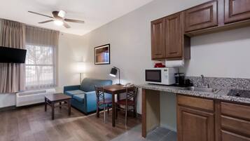 A compact living space with a kitchenette, a dining area with a table and chairs, a sofa, a ceiling fan, and a window with curtains.