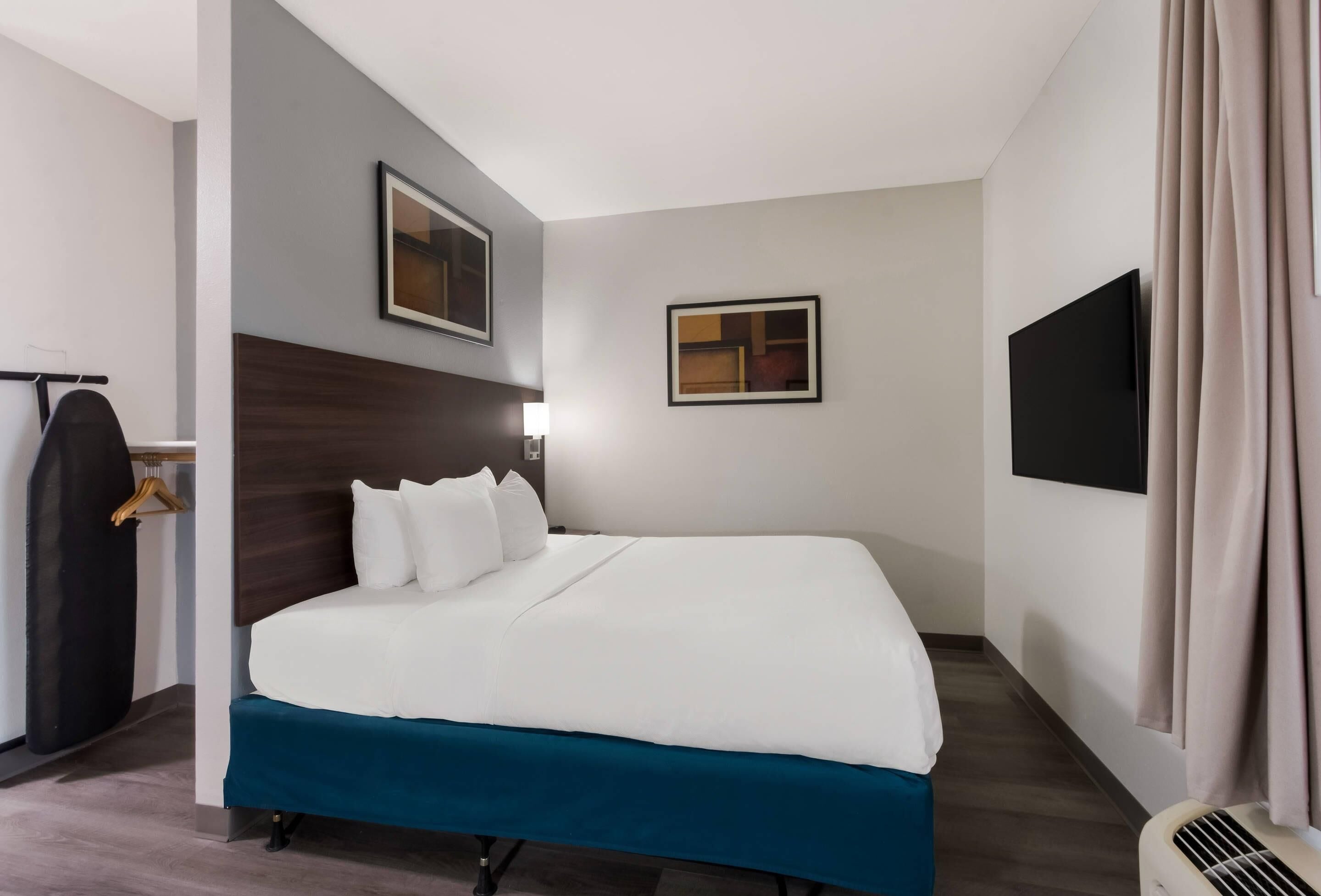 A hotel room with a bed, a wardrobe, a flat-screen TV, and a wall-mounted picture.