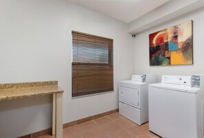 A laundry room with a washing machine, dryer, and a window with blinds. - MainStay Suites Extended Stay Hotel Casa Grande (Casa Grande)