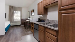 A compact hotel room with a kitchenette, a bed, a desk, and a window with curtains. - MainStay Suites Extended Stay Hotel Casa Grande (Casa Grande)