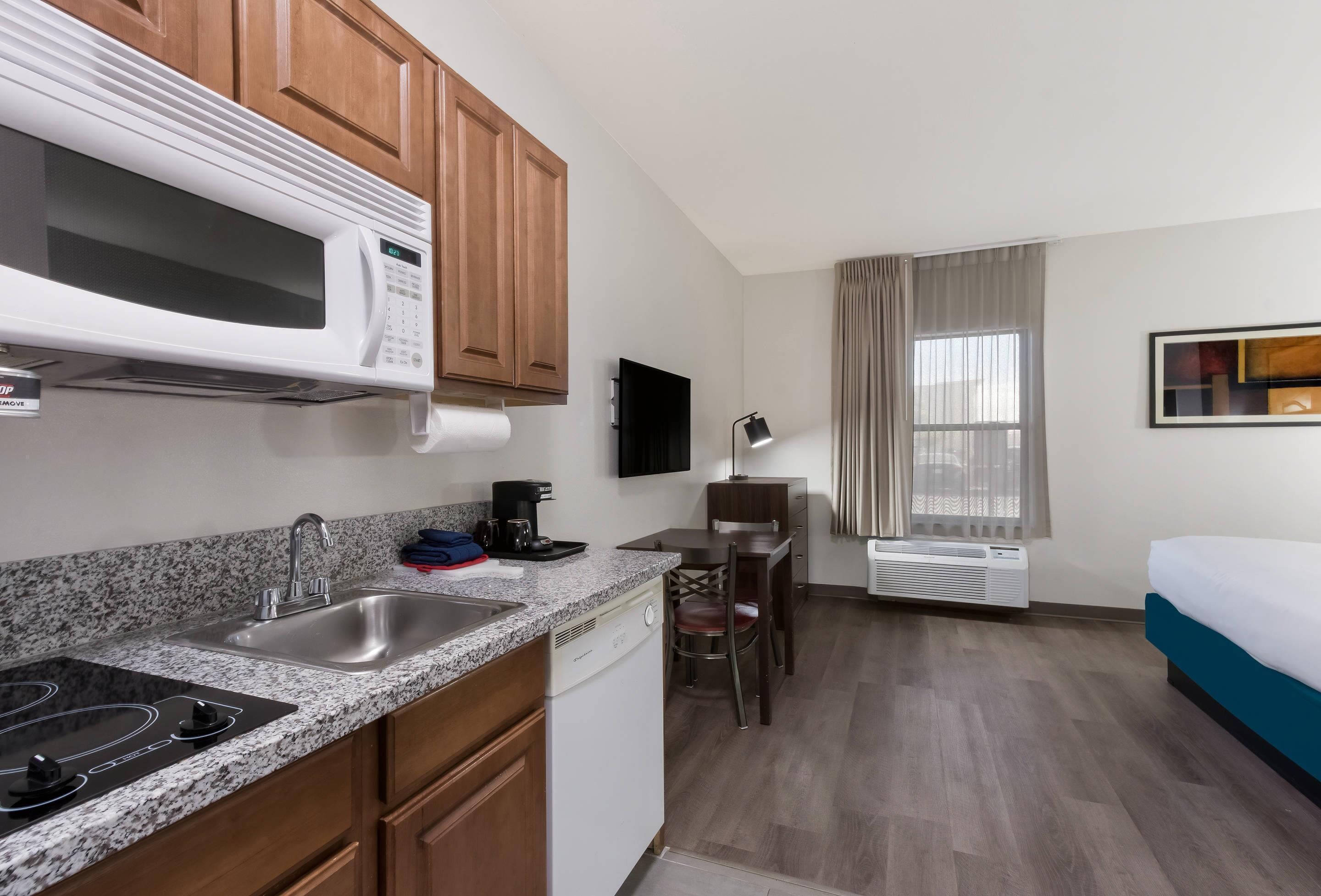 A compact hotel room with a kitchenette, a dining area, a bed, and a large window with curtains.