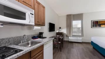 A compact hotel room with a kitchenette, a dining area, a bed, and a large window with curtains.