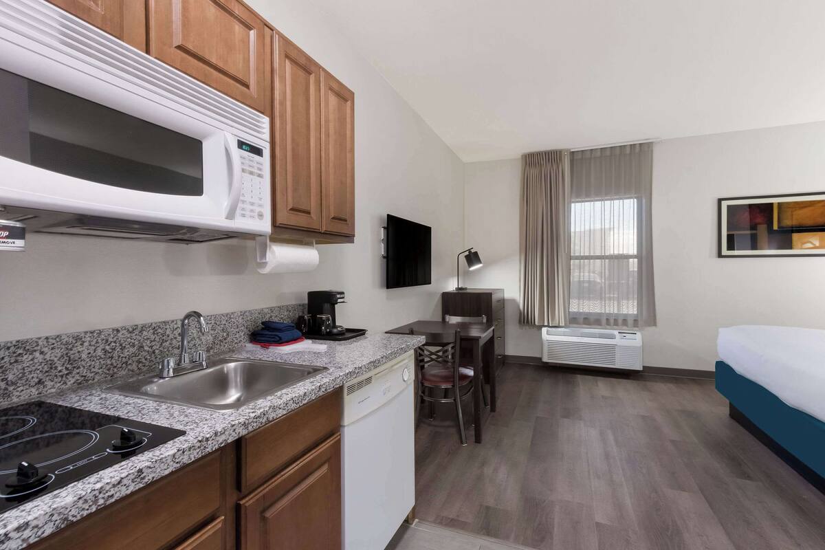 A compact hotel room with a kitchenette, a bed, a desk, and a TV.