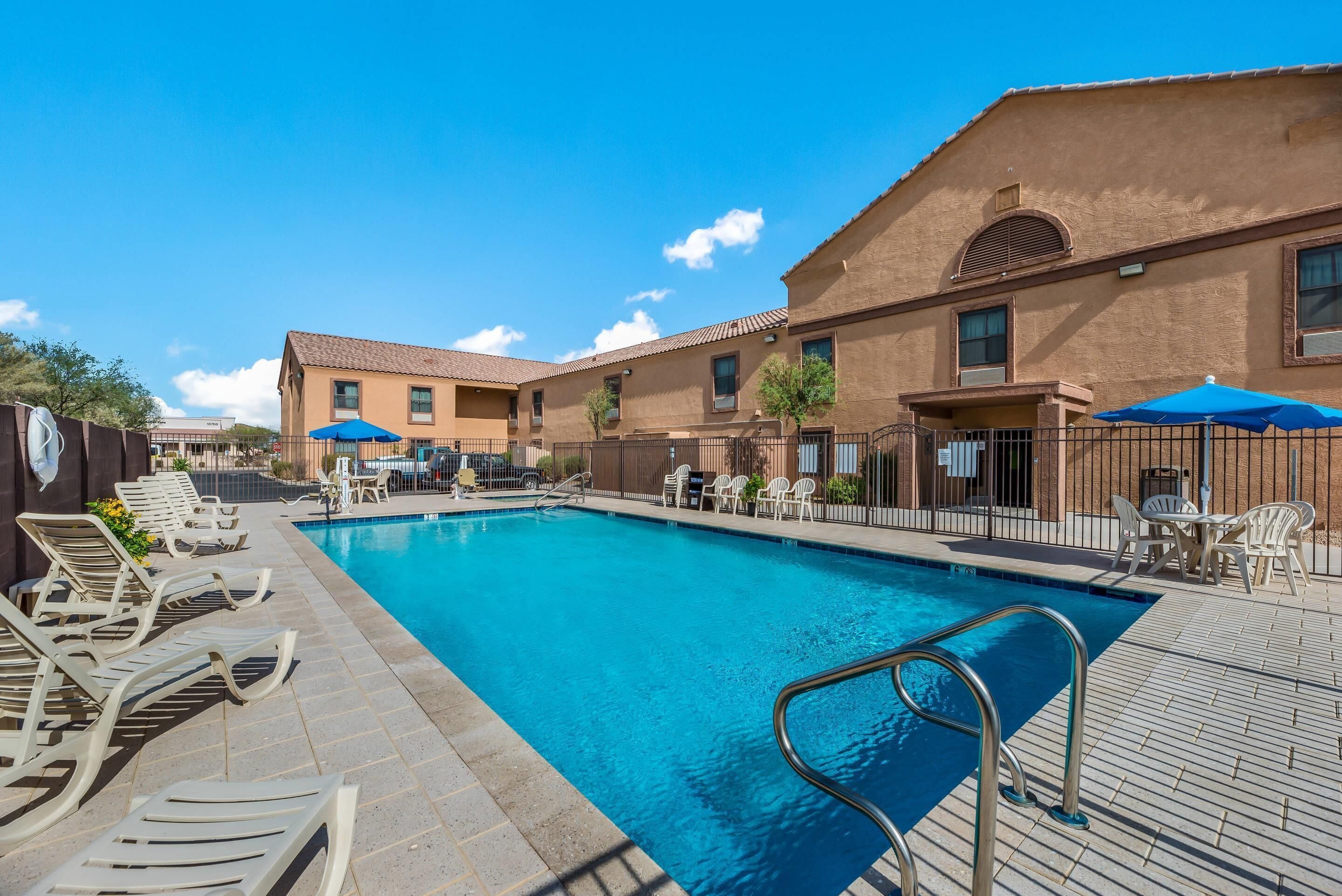 A swimming pool with lounge chairs and umbrellas, surrounded by buildings with a tiled roof.