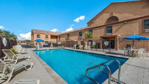 A swimming pool with lounge chairs and umbrellas, surrounded by buildings with a tiled roof. - MainStay Suites Extended Stay Hotel Casa Grande (Casa Grande)