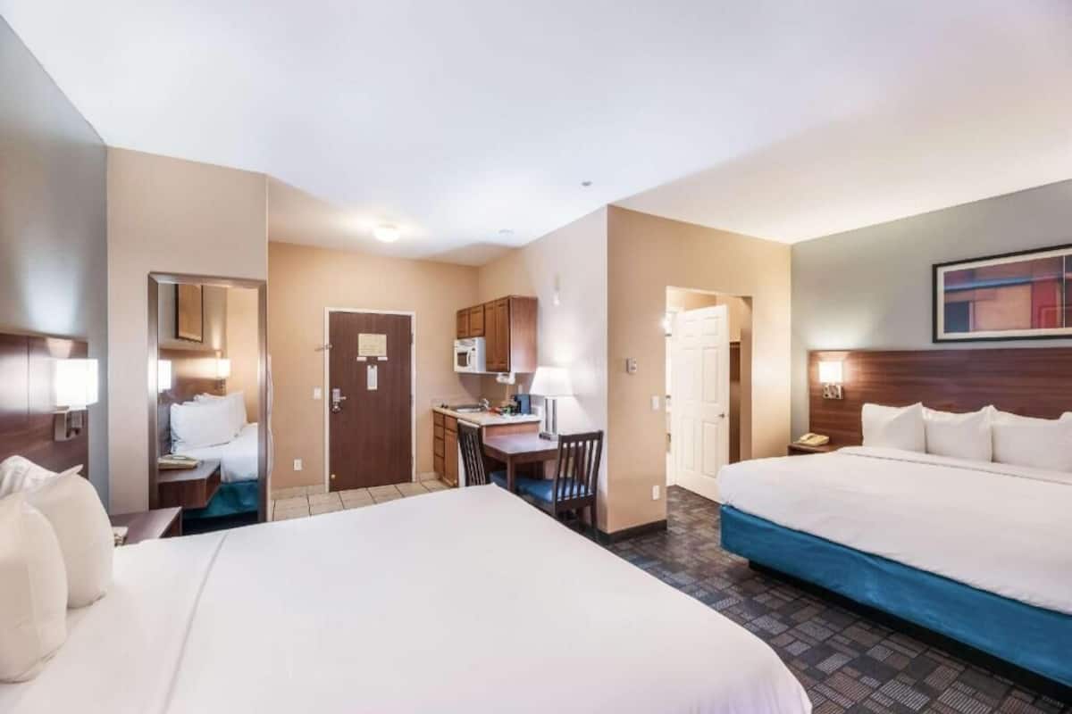 A hotel room with two beds, a desk, a microwave, and a small kitchenette.