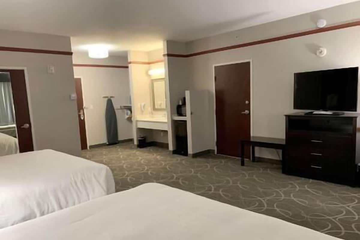 A hotel room with two beds, a dresser, a television, and a bathroom visible in the background.