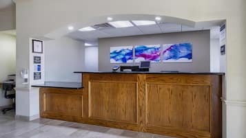 A reception desk with a wooden finish, a flat-screen monitor, and a phone. There are two framed artworks above the desk.