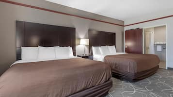 A hotel room with two beds, a nightstand, a lamp, and a wardrobe.