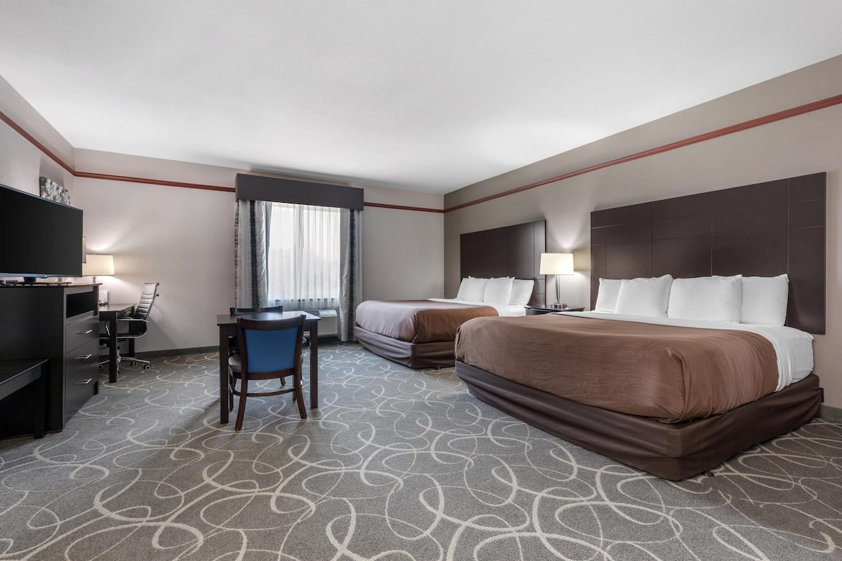 A hotel room with two beds, a desk with a chair, a television, and a window with curtains.