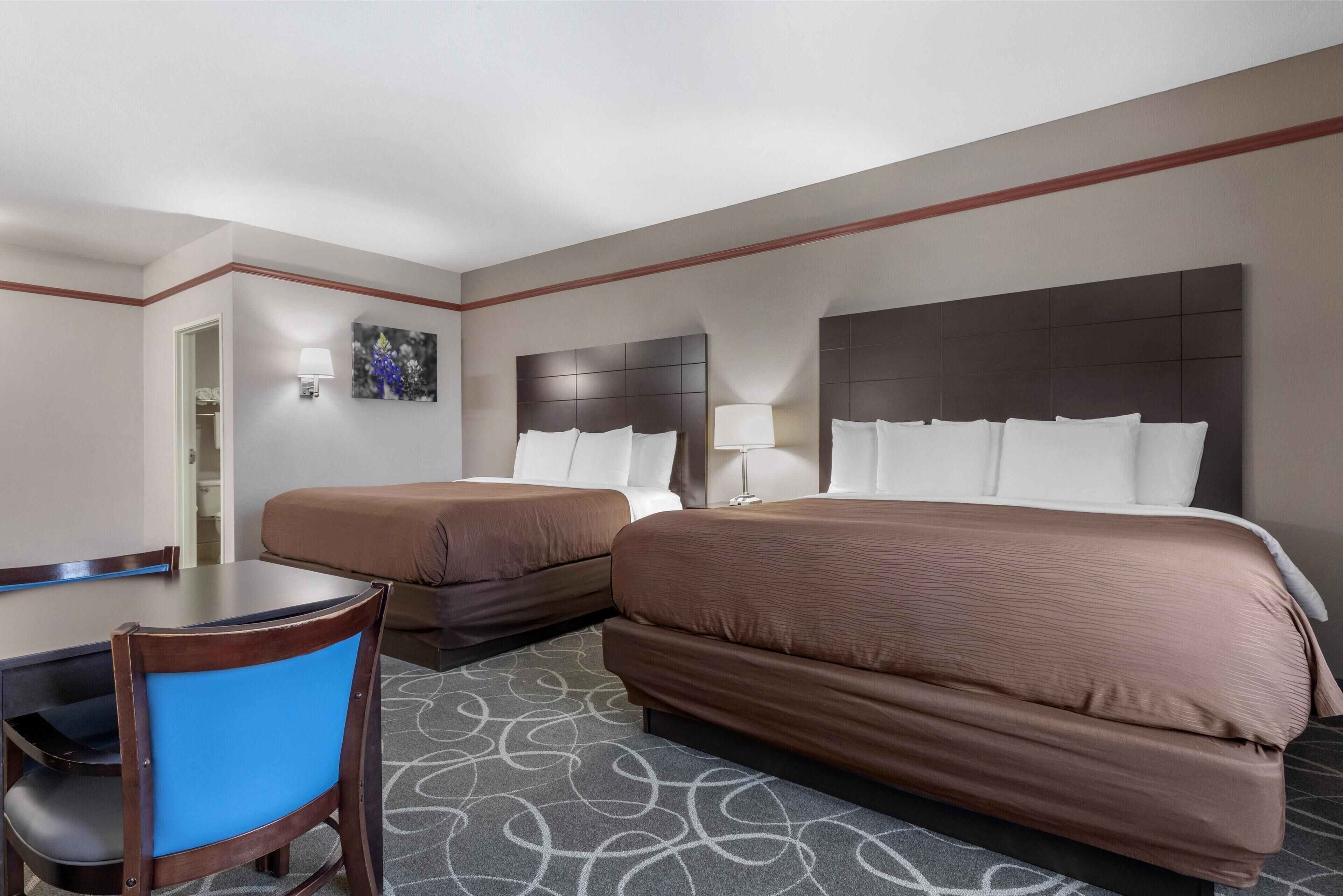 A hotel room with two beds, a desk, and a chair.