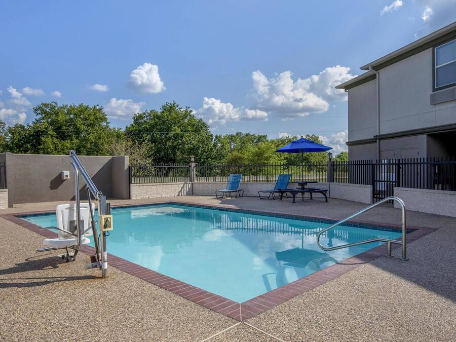 A swimming pool with a metal ladder, blue lounge chairs, and a blue umbrella.