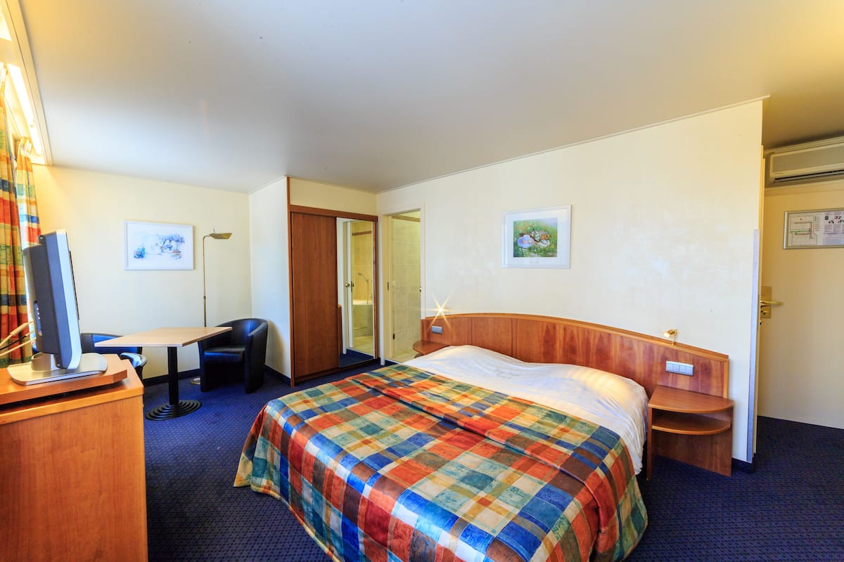 A hotel room with a bed, desk, chair, and a television.