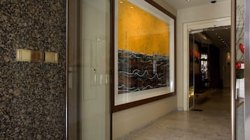 A hallway with a large abstract painting, a marble floor, and a door leading to another room.