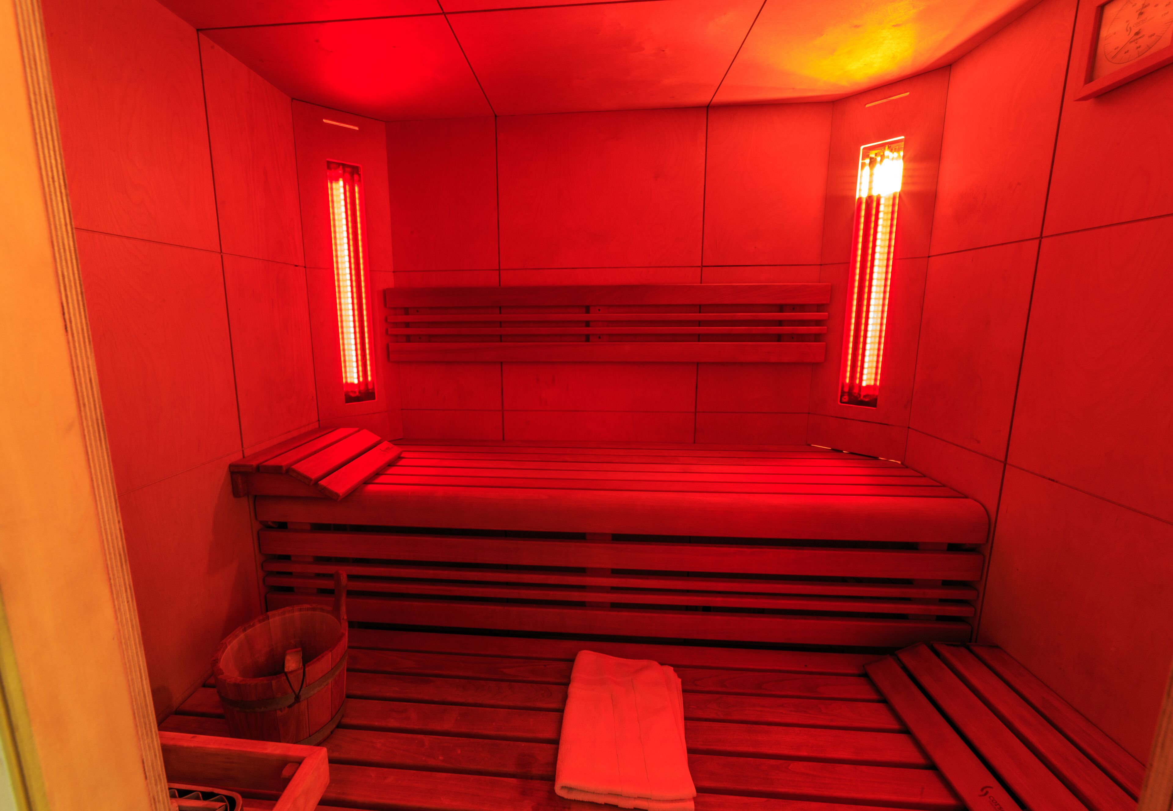 A sauna with benches and a bench seat, a towel, and a wooden bucket.
