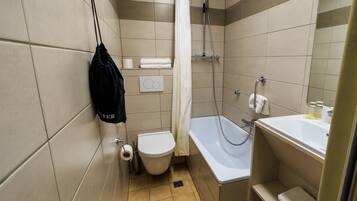 Une petite salle de bain carrelée, équipée de toilettes, d’une douche et d’un lavabo.