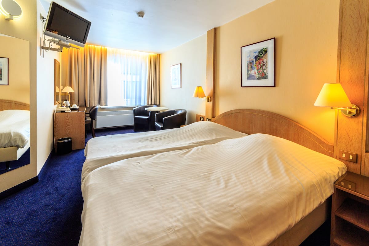 A hotel room with two beds, a desk, a chair, a TV, and a painting on the wall.