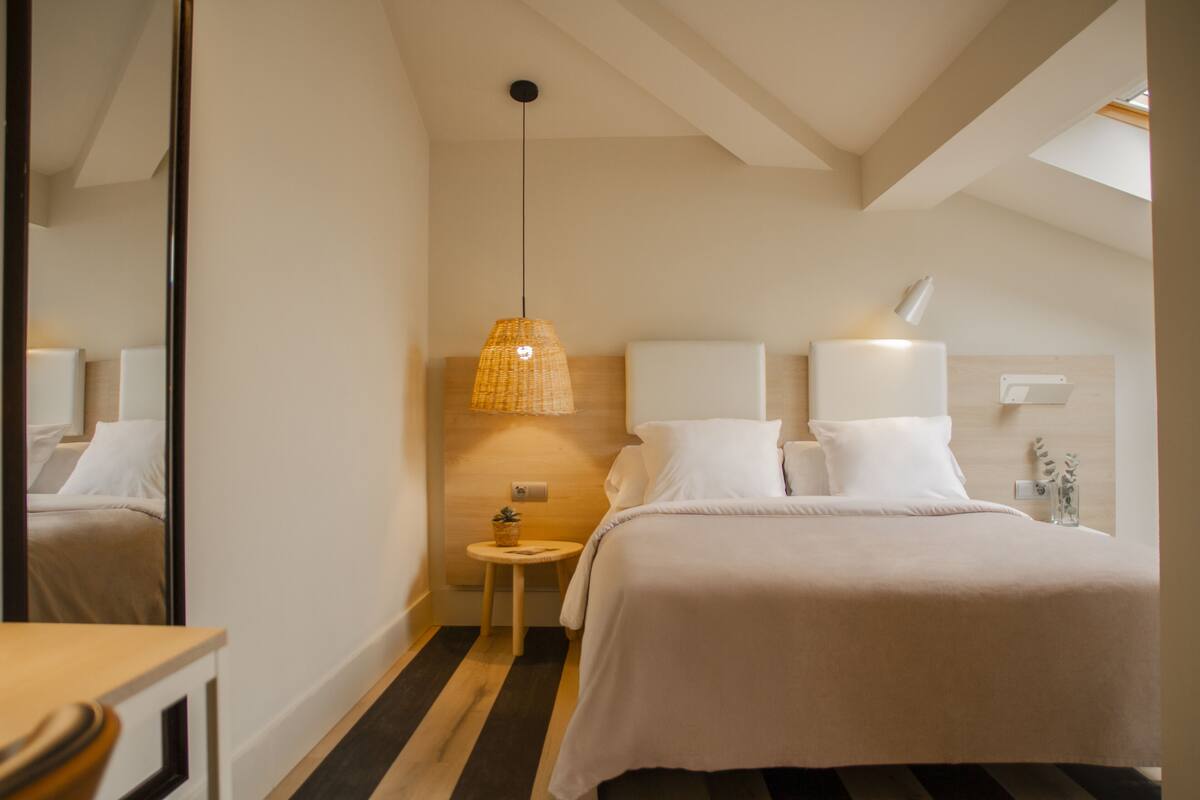 A hotel room with a bed, bedside table, lamp, and a small round table with a plant.