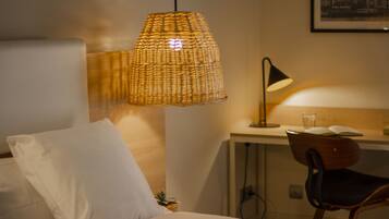 Een hotelkamer met een bed, een bureau, een stoel, een lamp en een wandplank met een plant.