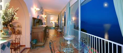 Un balcone con tavolo e sedie in vetro, vista sul mare e una zona pranzo con tavolo e sedie.